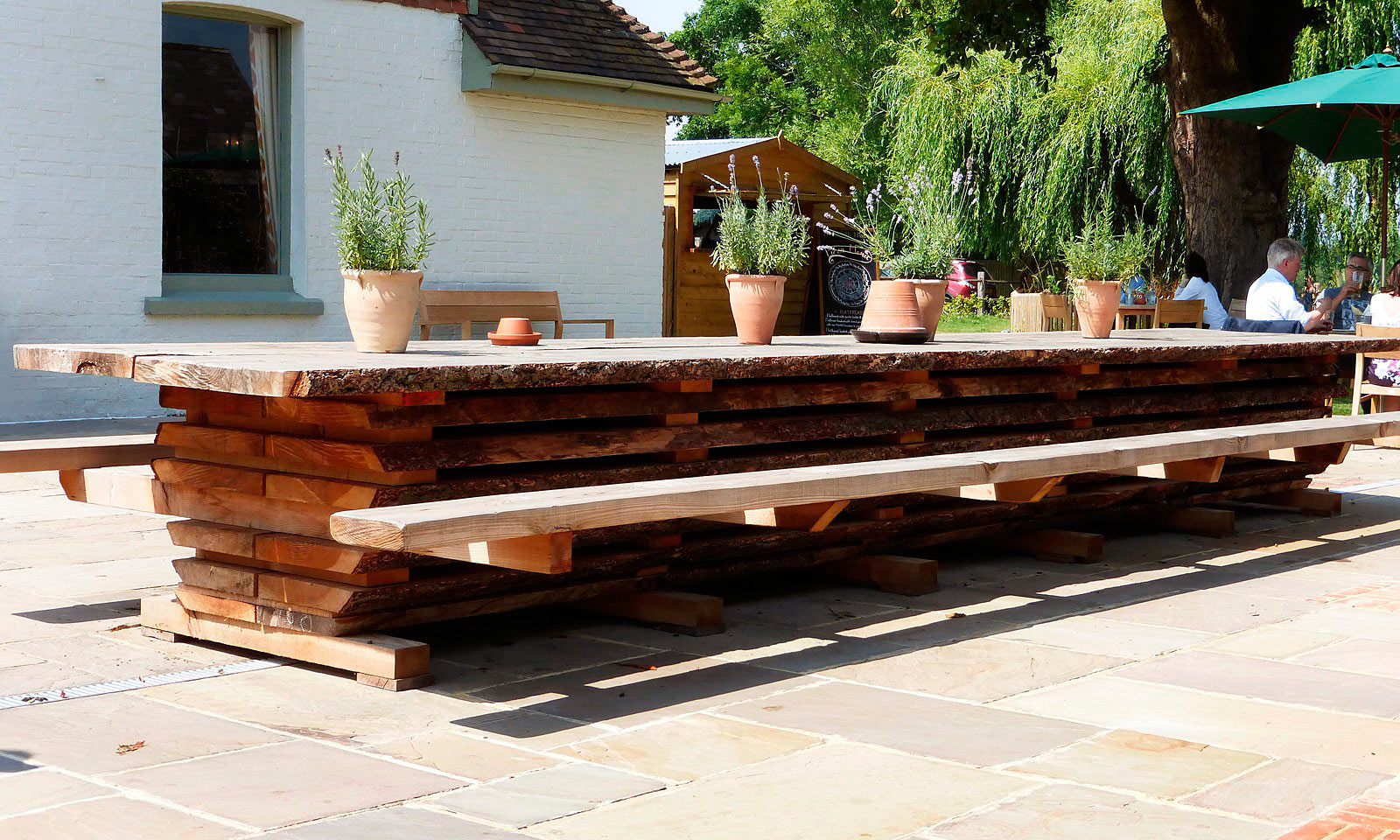 Milk House Table. A bespoke, unique 7m garden table that seats 35 people and is installed at the Milk House pub in Sissinghurst. Handmade using a whole Douglas Fir tree and manufactured by the skilled joiners at Mounts Hill Woodcraft.